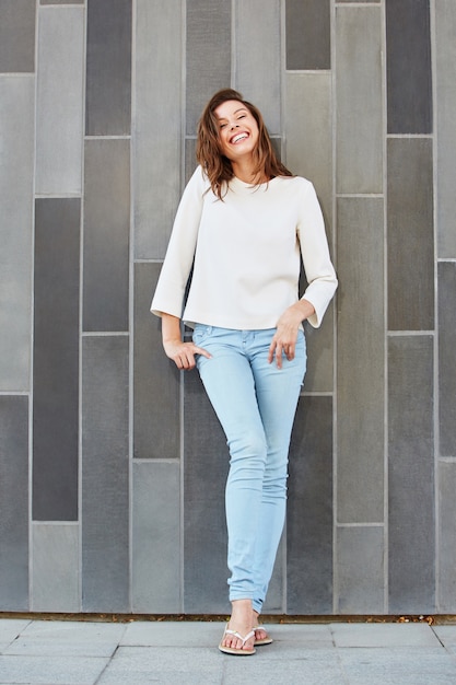 Beautiful young woman leaning against wall and smiling 