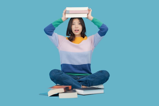 Photo a beautiful young woman lifts many books on her head while smiling happily