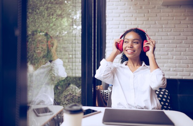 Beautiful young woman listening to music with headphones and drinking coffee in a cafe