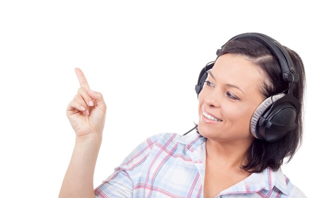 Beautiful Young Woman Listening Music with Headphones and Pointing Finger to Empty Space on a white background