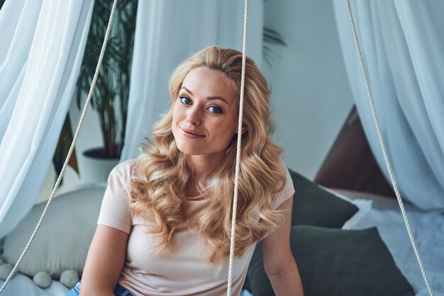 Beautiful young woman looking at camera and smiling while sitting on bed at home