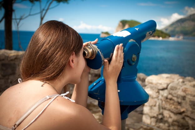 Beautiful young woman looking on mountain through touristic telescope