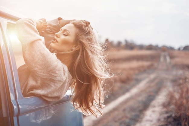 Beautiful young woman looking out of the window while enjoying road trip in minivan