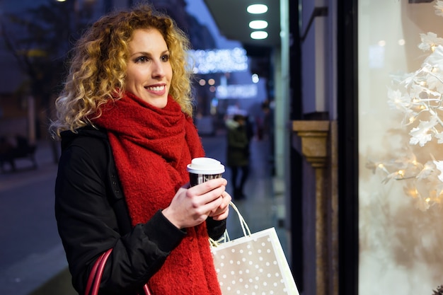 Beautiful young woman looking at the shop window at night.