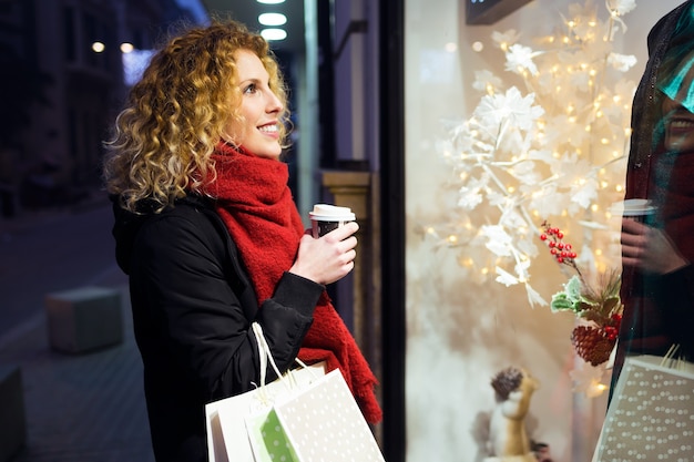 Photo beautiful young woman looking at the shop window at night.