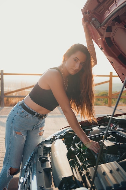 美しい若い女性は夕暮れ時に車のエンジンを見る