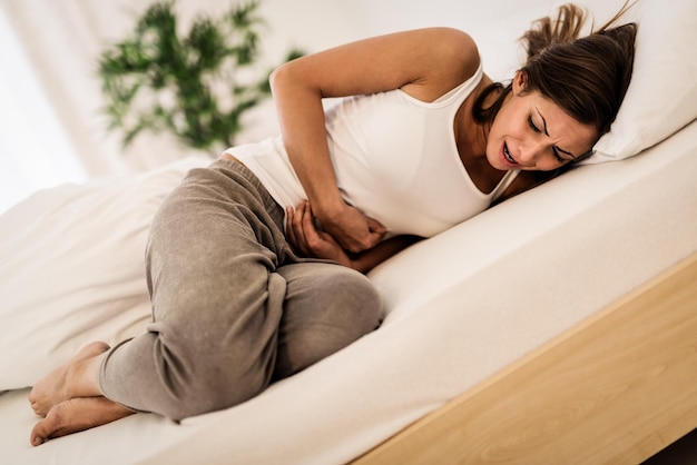 Beautiful young woman lying on bed and holding hands on her stomach.