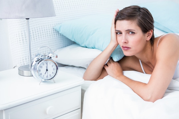 Beautiful young woman lying in bed with alarm clock 