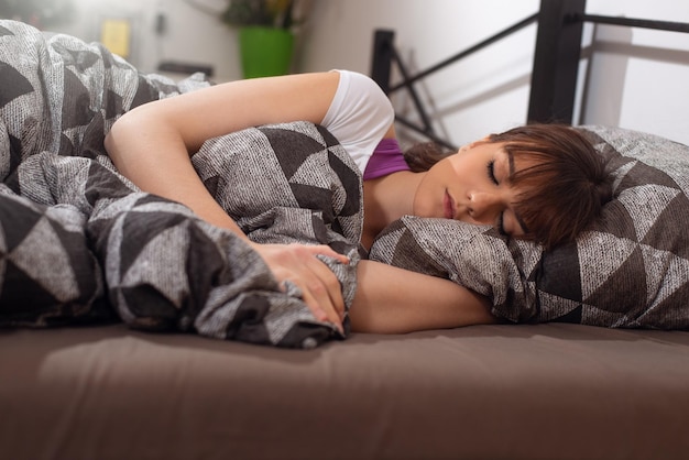 眠っている手に頭を休んで毛布の下の枕の上に白いベッドで横になっている美しい若い女性