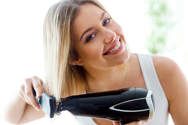 Beautiful young woman making hairstyle near mirror in the bathroom at home.