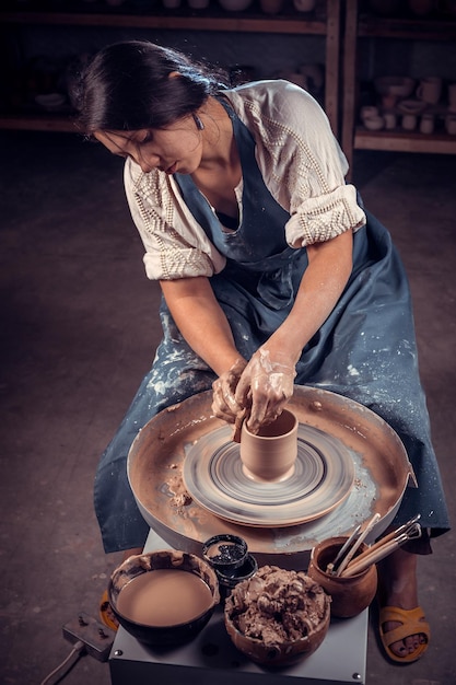 Beautiful young woman master shows how to work with clay and pottery wheel. Handmade products.