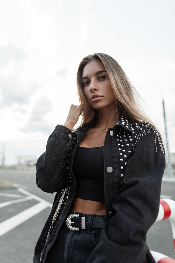 Photo beautiful young woman model with blonde hair with a pretty face in a fashion black denim jacket and a black top t-shirt with black jeans with a belt walks in the city