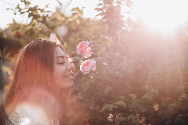 Beautiful young woman near a bush of pink roses