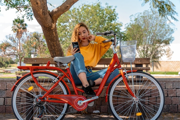 Beautiful young woman outdoors in park with bicycle beautiful spring day using mobil phone