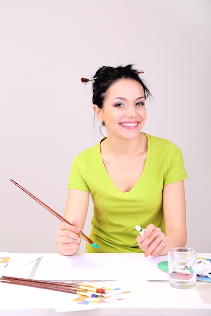 Beautiful young woman painter at work on color background