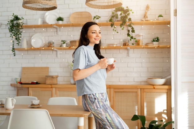 キッチンでお茶を飲むパジャマの美しい若い女性