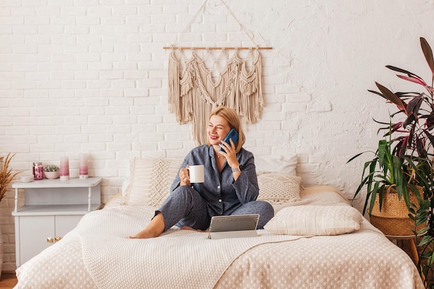 Beautiful young woman in pajamas working on a laptop in bed talking on the phone Online shopping