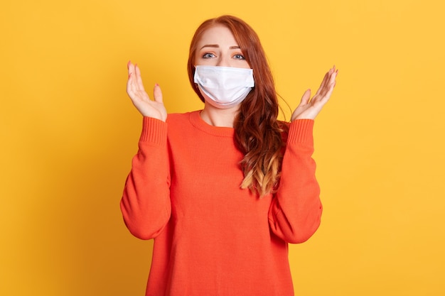 Beautiful young woman in panic about flu, posing isolated over yellow wall with raising hands