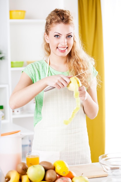 Beautiful young woman peeling apple in a kitchen.  Looking at camera.