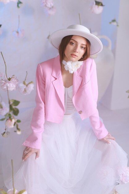 Beautiful young woman in pink colors and blonde hair on a background of blooming roses Spring girl