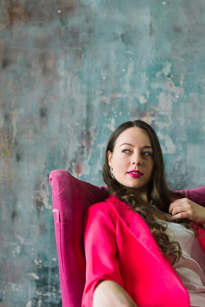 Beautiful young woman in pink suit sitting on pink chair in loft interior