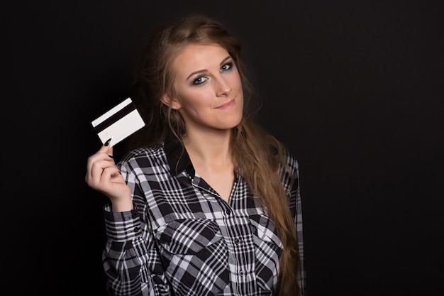 Beautiful young woman in plaid shirt and with long fair-haired hair holds a credit card smiling