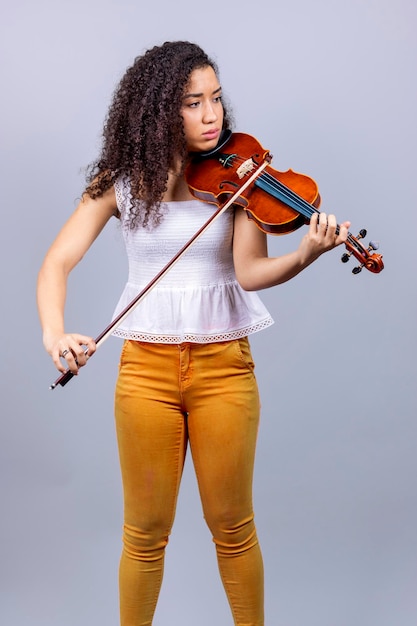 Beautiful young woman playing violin over gray