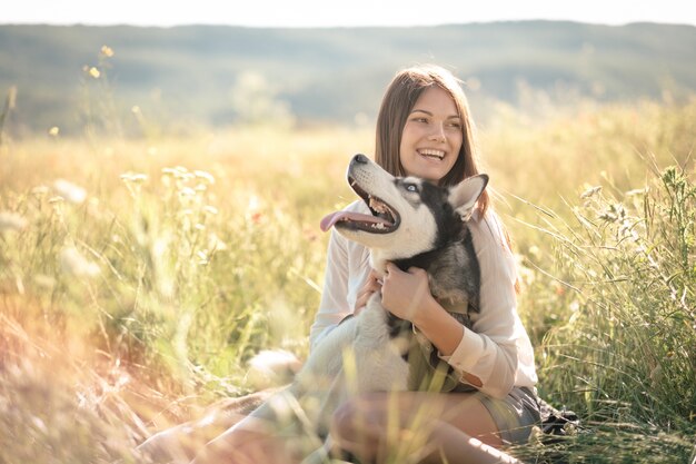 屋外の公園で面白いハスキー犬と遊ぶ美しい若い女性