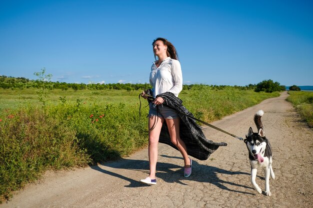 屋外の公園で面白いハスキー犬と遊ぶ美しい若い女性