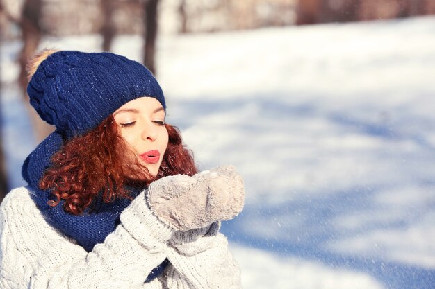 Beautiful young woman playing with snow outdoors on winter day