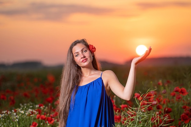 暖かい夕日の光の中でケシ畑に立ちながら太陽の玉で遊ぶ美しい若い女性