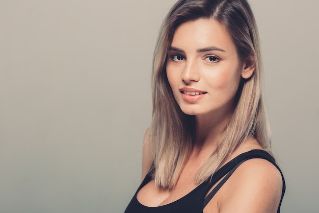 Beautiful young woman portrait in black shirt smiling posing attractive blond. Studio shot. Gray background.