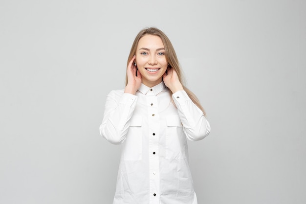 Beautiful young woman portrait Portrait of a beautiful smiling blonde in white shirt on a whitegray woman straightens her hair or holds her head