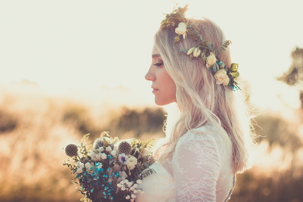 Bellissimo ritratto di giovane donna in abito bianco in stile boho con una ghirlanda floreale in estate