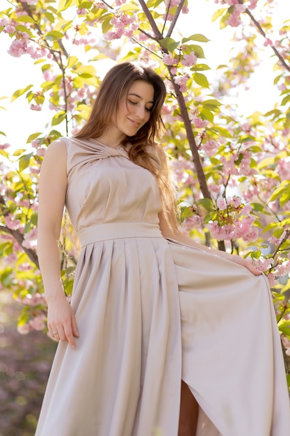 Beautiful young woman posing in a blooming sakura garden.