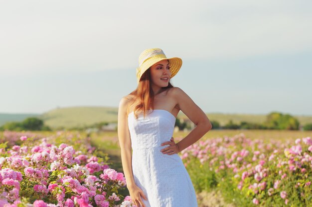 Beautiful young woman posing near roses in a garden.