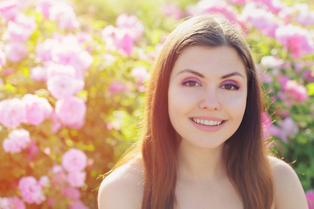 Красивая молодая женщина позирует возле розы в саду.