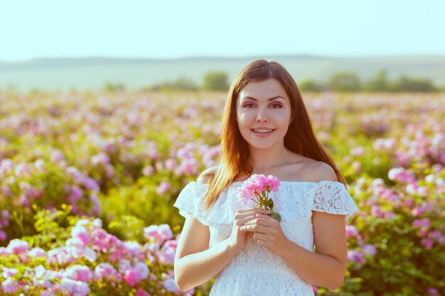 Beautiful young woman posing near roses in a garden.