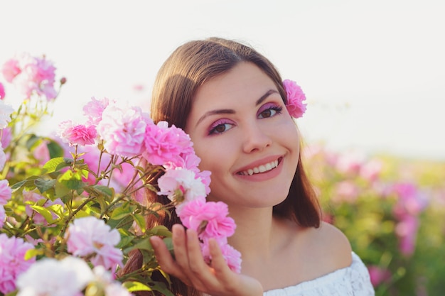 Beautiful young woman posing near roses in a garden.