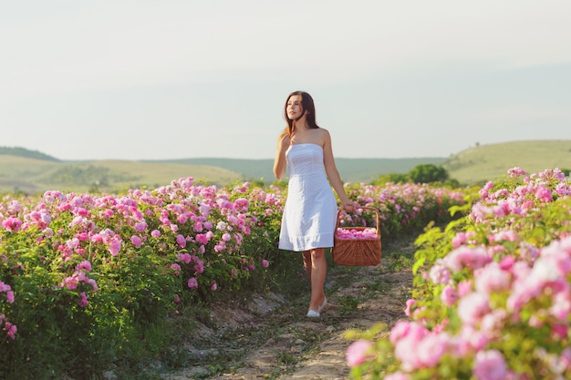 Beautiful young woman posing near roses in a garden.