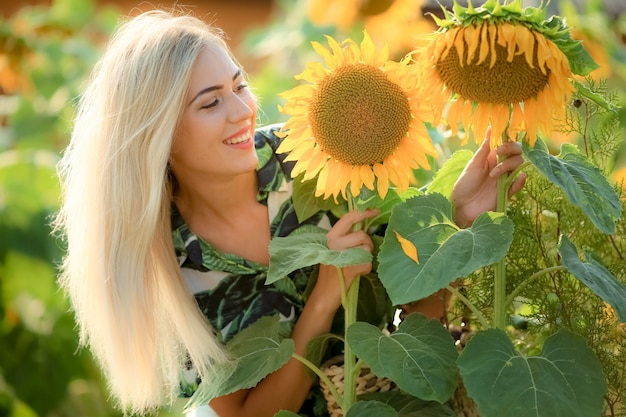 美しい若い女性が太陽の花に近いポーズします。フィールドでの夏の肖像画。ひまわりと美容分野で幸せな女。サンフレア、太陽光線、輝く太陽。巻き毛のブロンドの女性