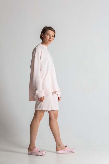 Beautiful young woman posing in a pink sweatshirt and shorts on the white studio background