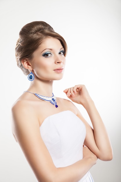 The beautiful young woman posing in a wedding dress. Beauty make-up. Jewellery