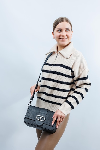 Beautiful young woman posing on a white background with a black handbag over her shoulder A woman is holding a black leather shoulder bag Women's fashion concept