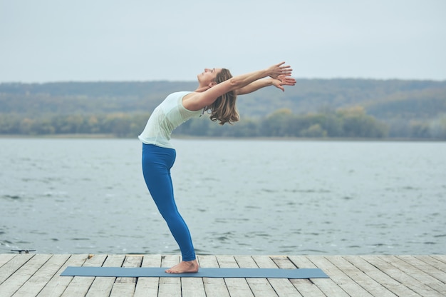 Beautiful young woman practices yoga asana Ardha Chakrasana