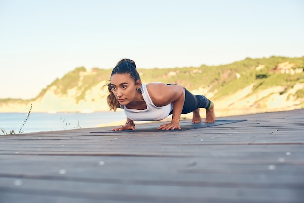 Photo beautiful young woman practicing yoga on seaside against blue sea.