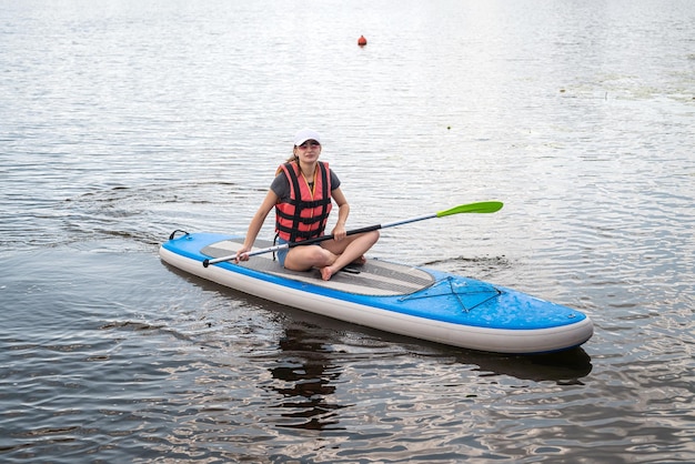 Beautiful young woman in a protective vest learns to swim on a sup board on a city lake active lifestyle summer time