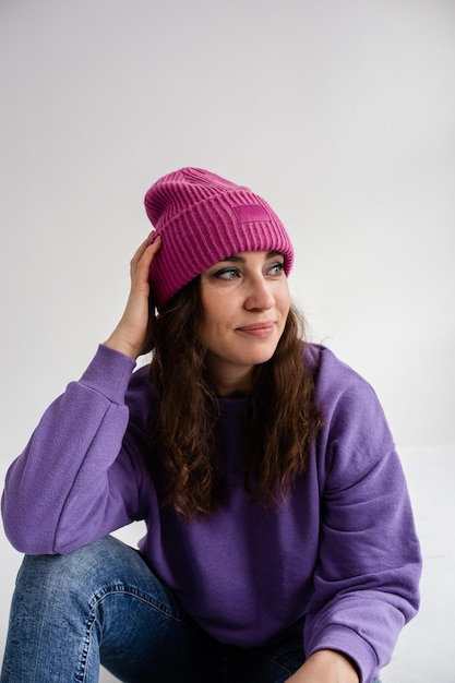スタジオで灰色の背景に紫色の帽子とトレーナーの美しい若い女性