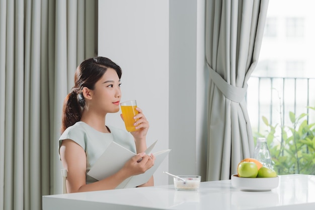 Beautiful young woman reading book during breakfast at home