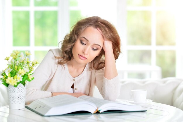 Beautiful young woman reading book in light cozy kitchen